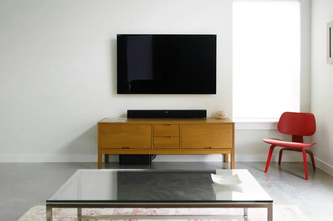 A wall-mounted flat-screen TV above a wooden media console in a white room, the kind of 4K screen KenoaTV plays on